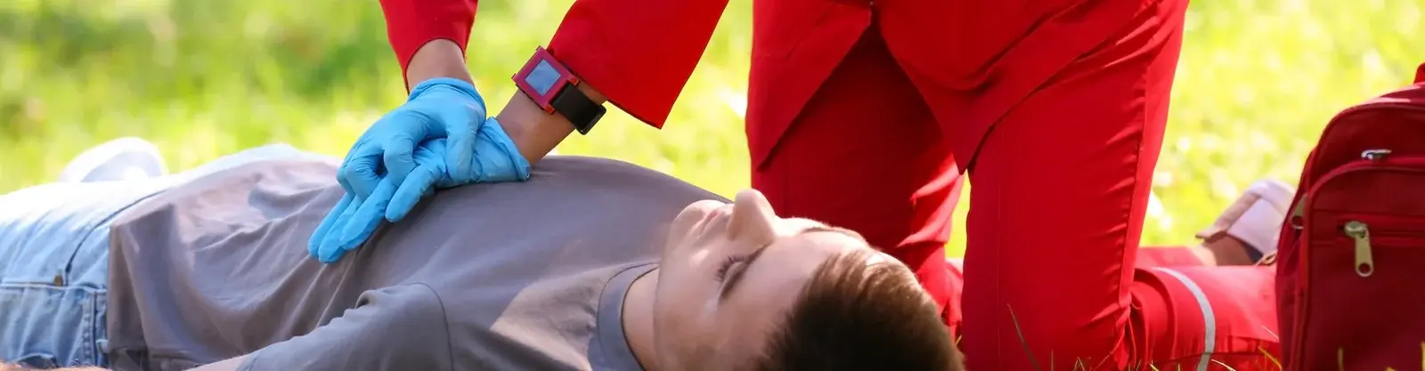 person receiving cpr chest compressions from a responder wearing gloves outdoors on grass